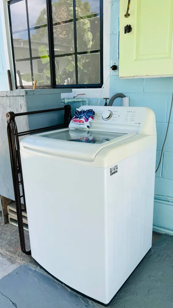 A top-loading washing machine in the covered backyard area at Silverleaf Cottage.