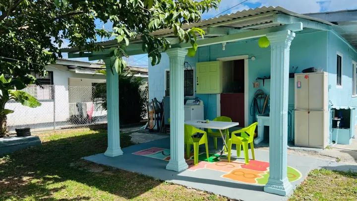 The blue cottage rear patio with lime-green chairs, an outdoor table and a leafy backyard.