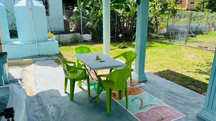 Covered backyard seating with four green chairs, a table and a view across the garden.