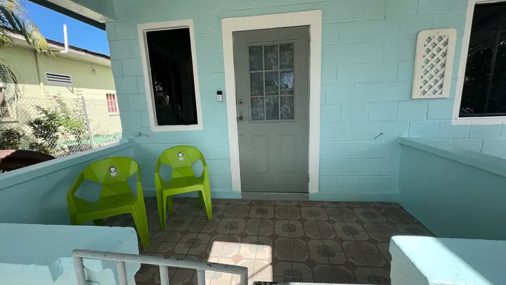 The covered porch with blue walls, a tiled floor and green chairs.